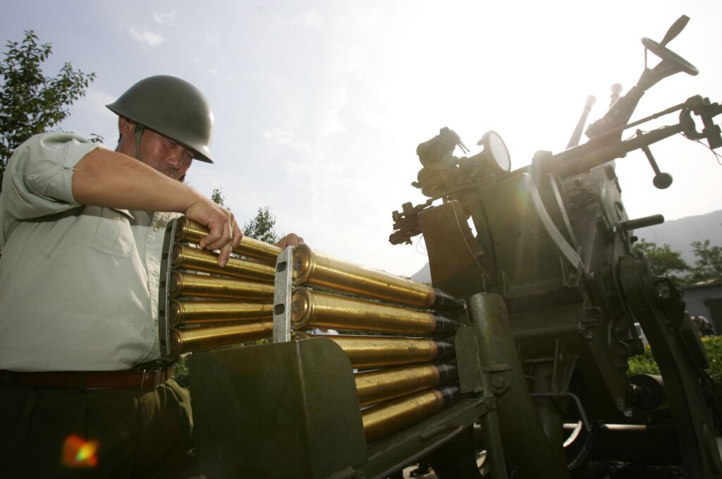 Солдат НОАК заряжает зенитное орудие снарядами с аэрозольными распылителями йодида серебра / ©China Photos, Bloomberg