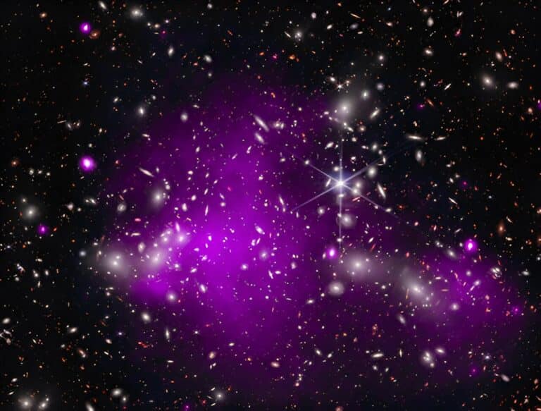 На этой иллюстрации совмещены рентгеновские данные обсерватории «Чандра» (фиолетовый) с инфракрасными данными телескопа «Джеймс Уэбб» (красный, зеленый, синий). Рекордная черная дыра находится в галактике UHZ1, которая расположена за скоплением галактик Abell 2744