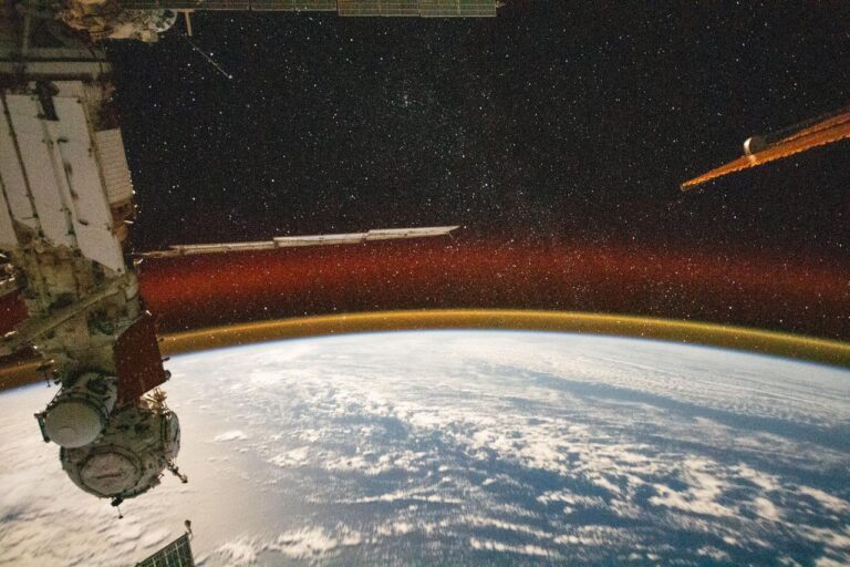 На этом снимке с высокой выдержкой, сделанном с борта МКС, видно свечение атмосферы Земли и звездное небо. Слева — научный модуль станции «Наука» и стыковочный модуль «Причал» / © NASA
